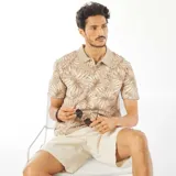 Remera tipo polo color beige con estampado de hojas en tonos marrones y blancos.