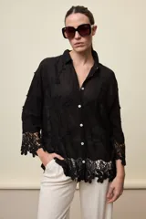 Camisa blanca de calce relajado, con cuello clásico, mangas 3/4 y cierre frontal de botones. Presenta bordados florales en relieve y detalles de crochet calado en los puños y el ruedo.
