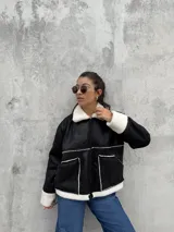 Campera tipo gamulán de color negro con interior y detalles de corderito en color blanco. Presenta cierre frontal, cuello clásico y dos bolsillos frontales.