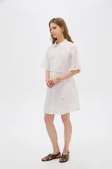 Vestido corto de algodón color blanco con diseño de broderie, cuello camisero, cierre frontal con botones, mangas cortas y lazo ajustable en la cintura.