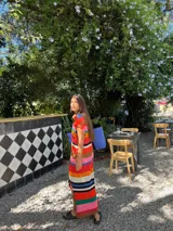 Vestido largo de tejido de punto, con rayas horizontales en tonos tierra, azul y blanco. Presenta cuello redondo, mangas cortas caídas y aberturas laterales en el ruedo.