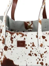 Cartera shopper confeccionada en cuero con pelo con estampado animal print tipo vaca en tonos blancos y marrones, con doble asa de hombro y bolsillo interior con cierre.