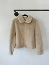 Chaqueta de piel sintética en color beige, con cuello clásico, cierre frontal metálico y ruedo con elástico ajustable. Cuenta con bolsillos laterales y mangas largas.