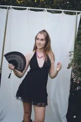 Vestido corto negro con escote en V profundo, estilo halter con tiras para atar al cuello. Presenta un diseño ajustado en el busto con tiras ajustables bajo el mismo que se cruzan y anudan en la espalda, y falda con volado en el ruedo con detalle de encaje.