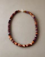 Collar artesanal compuesto por cuentas de concha Spóndylus talladas a mano en diversas formas y tonalidades cálidas, que van desde el púrpura y naranja hasta el blanco. Presenta un diseño asimétrico con cierre metálico.