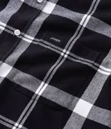 Camisa de franela de manga larga con estampado de cuadros en blanco y negro. Presenta cuello inglés, cierre frontal con botones y bolsillo en el pecho.