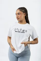 Remera blanca de algodón con estampa frontal en color negro que incluye iconos de café y la frase 'More coffee, please!'. Presenta cuello redondo y mangas cortas.