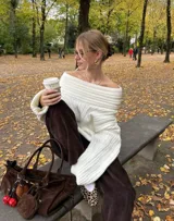 Buzo tejido de punto color crudo con diseño off-shoulder, textura acanalada y calce relajado.