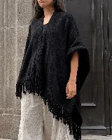Ruana negra de tejido artesanal en lana, de diseño amplio y asimétrico, con terminación de flecos hechos a mano en los bordes.