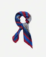 Pañuelo cuadrado de tela fina color blanco con lunares negros. Tiene un borde con franjas de color azul, rojo y azul marino.