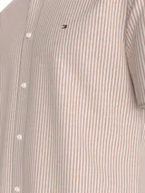 Camisa de manga corta Tommy Hilfiger confeccionada en tejido oxford de algodón. Presenta un diseño a rayas verticales en color naranja y blanco, cuello con botones y logo de la marca bordado en el pecho.