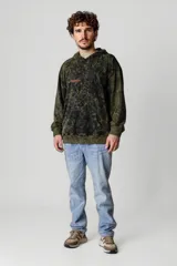 Canguro oversize con capucha, color verde militar con efecto tie-dye en negro y estampado con la palabra "Reason" en el pecho.