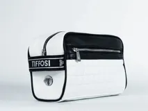 Necessaire Tiffosi de diseño rectangular, combinando paneles en color blanco y negro. Presenta un patrón acolchado tipo cuadrille en la parte inferior blanca, cierre superior con cremallera metálica y una banda lateral con el logo de la marca. Incluye un bolsillo frontal con cierre y un detalle metálico circular con el logo en el lateral.