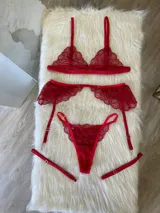 Conjunto de lencería de tres piezas en encaje rojo, compuesto por un bralette triangular, una tanga regulable y un portaligas con volados en las caderas.