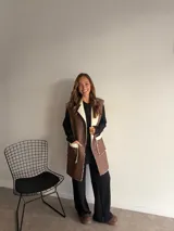 Chaleco largo de eco cuero color marrón con interior y detalles de corderito en solapas y bolsillos frontales.