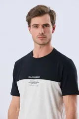 Remera de algodón y poliéster de corte clásico, con diseño en bloques de color negro en la parte superior y gris melange en la inferior. Presenta cuello redondo, mangas cortas y un pequeño estampado tipográfico en el pecho.