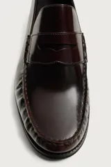 Mocasín de vestir color marrón oscuro, fabricado en cuero, con detalle de antifaz en el empeine y suela a tono con ligero tacón.
