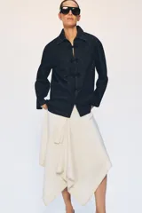 Chaqueta de denim azul oscuro con cuello solapa, manga larga y cierre frontal mediante alamares decorativos de estilo oriental.