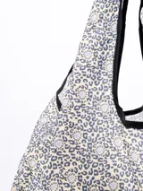 Bolsa de mandados de tela estampada con diseño floral en tonos celeste y blanco, con ribete negro en las asas.