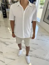 Camisa blanca de manga corta, cuello camisero y cierre frontal de botones.
