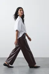 Pantalón de cuero sintético en color marrón oscuro, con corte flare, tiro medio y costuras frontales verticales que estilizan la silueta.