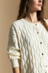 Cardigan de tejido tramado color blanco, con cuello redondo y cierre frontal de botones. Presenta un diseño con textura de ondas en relieve y mangas largas con puños ajustados.