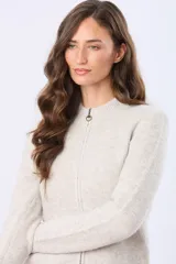 Campera tejida de punto con cierre frontal completo, cuello tipo mao y puños acanalados. Presenta un parche decorativo de cuero sintético en la parte inferior y un diseño de textura suave y abrigada.