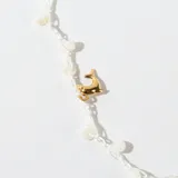 Collar corto con cadena de hilo blanco, cuentas de plástico color crema y dijes colgantes de metal dorado con forma de pez y estrellas de mar.