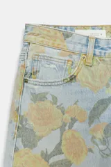 Jeans de tiro bajo confeccionados en denim, con diseño holgado y estampado integral de rosas en tonos amarillos y verdes sobre fondo celeste claro. Cuenta con cinco bolsillos, trabillas para cinto y botamangas con vuelta.