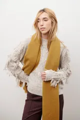 Buzo de punto color beige con cuello redondo, mangas largas con flecos decorativos y diseño de trenzas en el frente.