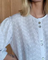 Camisa de jean celeste con cuello redondo, mangas abullonadas y puños elásticos. Cierre frontal con botones.