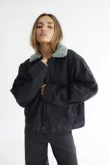 Campera bomber de denim azul oscuro con costuras a contratono en color verde. Presenta cuello de corderito en color marrón, cierre frontal y diseño holgado.