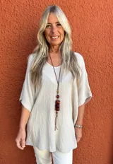 Blusa de corte holgado y diseño minimalista, confeccionada en tela texturizada color beige, con escote en V y mangas cortas tipo kimono.