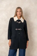 Montgomery de lana color negro con cuello de punto en color crema, cierre frontal con alamares y bolsillos con solapa.