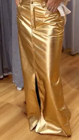 Falda larga dorada de cuero sintético, con corte recto, tiro alto, bolsillos laterales y abertura frontal.