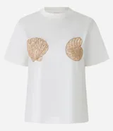 Remera de algodón color blanco con cuello redondo y mangas cortas. Presenta un bordado detallado de dos conchas marinas en color dorado en la parte frontal.