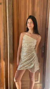Vestido corto dorado con lentejuelas, de un solo hombro, con breteles finos y falda irregular con capas y frunces.