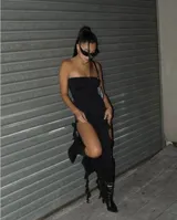 Vestido negro strapless con tajo alto lateral y detalles de tiras colgantes.