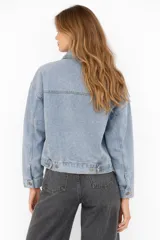 Campera de jean color negro con cierre frontal de botones metálicos, cuello clásico, bolsillos frontales con solapa y mangas largas.