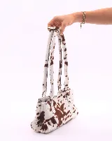 Cartera tipo baguette confeccionada en cuero vacuno con pelo y estampado animal print de vaca. Presenta doble asa de hombro, cierre superior y broches laterales para ajustar su volumen.