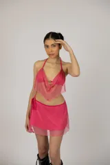 Conjunto de dos piezas compuesto por un top estilo halter con escote drapeado y una minifalda con lazo lateral ajustable. Ambas prendas están confeccionadas en tejido de malla con acabado brillante y glitter.