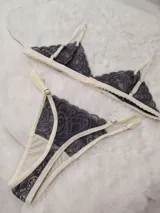 Conjunto de lencería de encaje gris oscuro con detalles en tono marfil, compuesto por un soutien triangular y bombacha a juego.