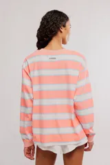 Remera manga larga de algodón con diseño de rayas horizontales en tonos verdes, azul marino, rosado y celeste. Presenta cuello redondo y un pequeño parche decorativo en el borde inferior.