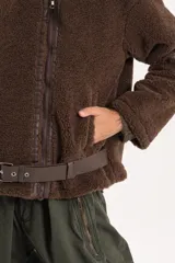 Chaqueta tipo gamulán de textura de corderito en color marrón, con cierre frontal, solapas amplias y detalles de correas ajustables en la cintura y mangas.