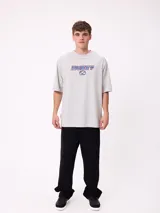 Remera de corte holgado color gris melange, con mangas raglán y estampado frontal con el logo de la marca Rusty en tonos azul y rojo.