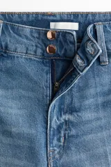 Jean de tiro alto con pierna amplia y corte holgado. Presenta cierre frontal con doble botón, bolsillos traseros de parche y pliegues marcados en el frente y la parte posterior.