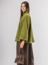 Chaqueta tipo capa confeccionada en paño, con cuello alto, cierre frontal de botones grandes y mangas amplias. Cuenta con bolsillos laterales y forro interior.