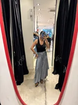 Pantalón de corte amplio y fluido, color gris con acabado satinado, con cintura elástica y lazo ajustable. Presenta un diseño con paneles laterales que aportan volumen y movimiento.
