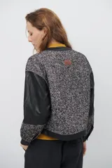 Chaqueta de diseño combinado con paneles de tejido de espiga en tonos marrones y burdeos, y paneles de cuero marrón en mangas y bordes. Presenta cuello redondo, cierre frontal con botones metálicos a presión y bolsillos delanteros.