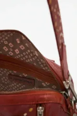 Bolso de mano tipo doctor bag o bowling bag, color marrón cuero, con diseño acolchado en rombos y tachas doradas. Posee doble asa de mano y un dije colgante de flecos largos de cuero marrón.